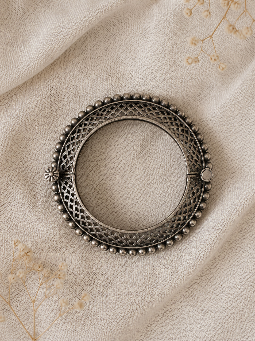 Decorative metal ring with intricate design on a beige fabric background